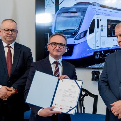 Wicemarszałek Województwa Śląskiego Grzegorz Boski podpisuje dokument, a obok stoją prezes Kolei Śląskich Krzysztof Klimosz i wiceprezes firmy Newag, Józef Michalik. (wygenerowano przez AI)