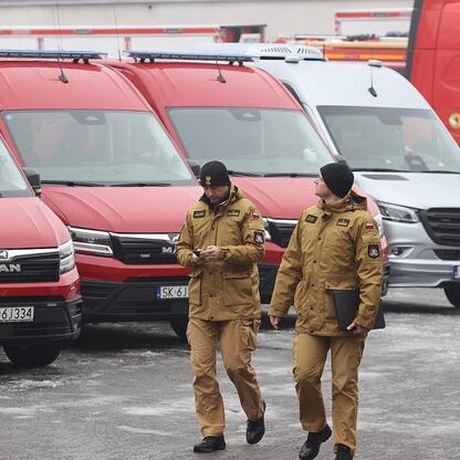 Dwóch pracowników w mundurach spaceruje przed czołgami ratowniczymi i strażackimi w Częstochowie, Polska. (wygenerowano przez AI)