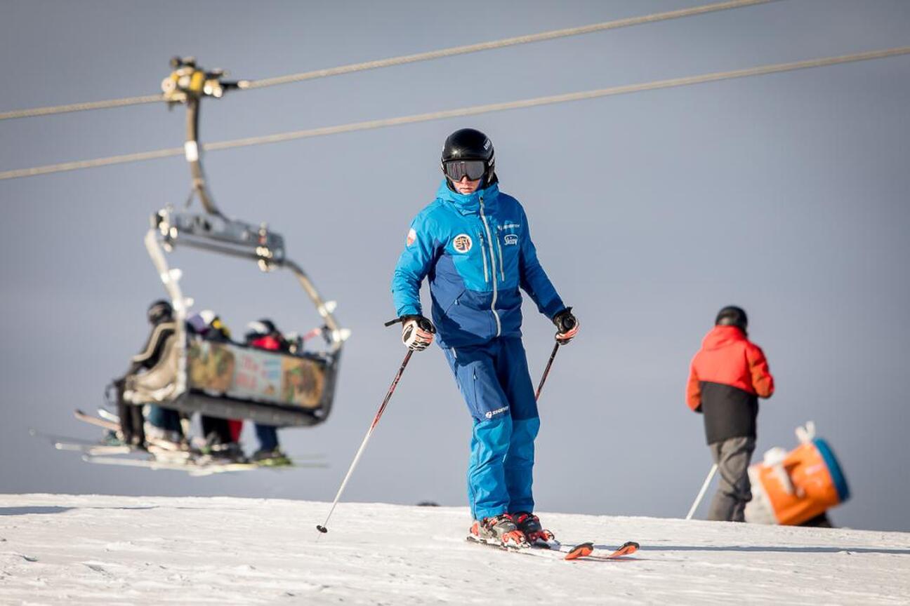 Skier w niebieskim kombinezonie stoi na śnieżnym stoku, trzymając narty, z tyłu widoczna kolejka narciarska. (wygenerowano przez AI)