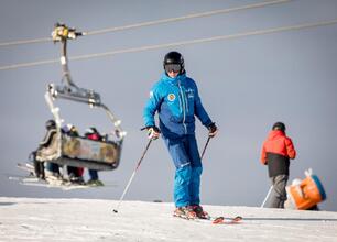 Skier w niebieskim kombinezonie stoi na śnieżnym stoku, trzymając narty, z tyłu widoczna kolejka narciarska. (wygenerowano przez AI)