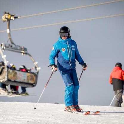 Skier w niebieskim kombinezonie stoi na śnieżnym stoku, trzymając narty, z tyłu widoczna kolejka narciarska. (wygenerowano przez AI)