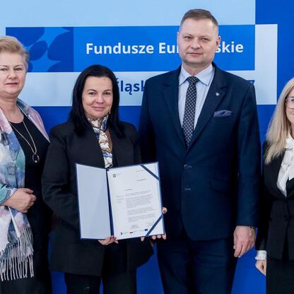 Członek Zarządu Województwa Śląskiego Rafał Adamczyk wręcza beneficjentom listy gratulacyjne, potwierdzające dofinansowanie projektów edukacji przedszkolnej. (wygenerowano przez AI)