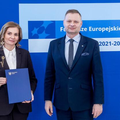 Rafał Adamczyk i nieznana osoba przedstawiają projekt dofinansowania funduszy europejskich dla przedszkoli w Śląsku. (wygenerowano przez AI)