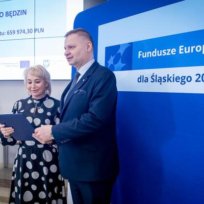 Członek Zarządu Województwa Śląskiego Rafał Adamczyk wręcza listy gratulacyjne uczestnikom projektów edukacyjnych dofinansowanych z Funduszy Europejskich dla Śląska 2021-2027. (wygenerowano przez AI)