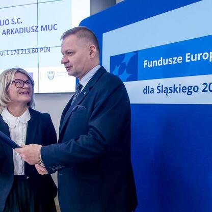 Członek Zarządu Województwa Śląskiego Rafał Adamczyk prezentuje dokument przed beneficjentką projektu 
