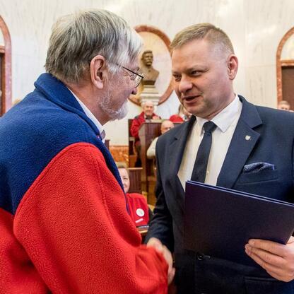 Członek Zarządu Województwa Śląskiego Rafał Adamczyk wręcza nagrodę przewodnikowi turystycznemu w Sali Sejmu Śląskiego. (wygenerowano przez AI)