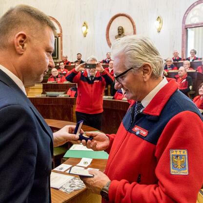 Członek Zarządu Województwa Śląskiego Rafał Adamczyk wręcza medal przewodnikowi z PTTK Pszczyna, podkreślając znaczenie turystyki w regionie. (wygenerowano przez AI)
