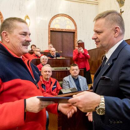 Członek Zarządu Województwa Śląskiego Rafał Adamczyk wręcza nagrodę przewodnikowi turystycznemu w Sali Sejmu Śląskiego. (wygenerowano przez AI)