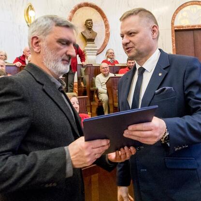 Członek Zarządu Województwa Rafał Adamczyk i Marcin Ryś uczestniczą w ceremonii wręczenia nagród za promocję turystyki w Sali Sejmu Śląskiego. (wygenerowano przez AI)