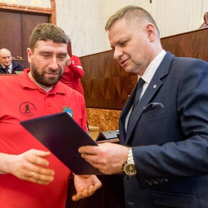 Członek Zarządu Województwa Rafał Adamczyk wręcza nagrodę na uroczystości w Sali Sejmu Śląskiego. (wygenerowano przez AI)