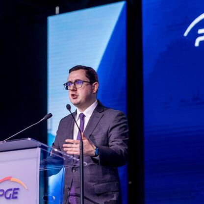Na podium przed PGE logo stoi mężczyzna w garniturze, gestykulując podczas przemówienia. (wygenerowano przez AI)