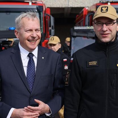 Dwóch mężczyzn przed strażackim pojazdem, Marszałek Województwa Śląskiego Wojciech Saługa i inny w mundurze. (wygenerowano przez AI)