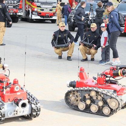 Zebrała się grupa ludzi wokół czerwonego i czarnego robotu ratowniczego, podczas demonstracji sprzętu strażackiego w Katowicach, Śląsk. (wygenerowano przez AI)