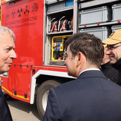 Marszałek Wojciech Saługa i uczestnicy spotkania przed czerwonym samochodem ratownictwa chemicznego. (wygenerowano przez AI)