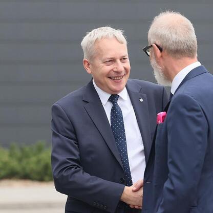 Dwóch mężczyzn w strojach formalnych trzyma się za ręce przed nowoczesnym budynkiem, podczas prezentacji planu inwestycyjnego TAURON dla Śląska. (wygenerowano przez AI)