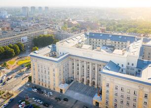 Aerial view of a grand, multi-story building with classical architecture, likely a significant public or governmental structure, situated in a bustling urban area. (wygenerowano przez AI)