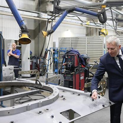 Marszałek Wojciech Saługa inspektuje metalowy rám w fabryce, wspierając inwestycję w produkcję pojazdów Legwan. (wygenerowano przez AI)