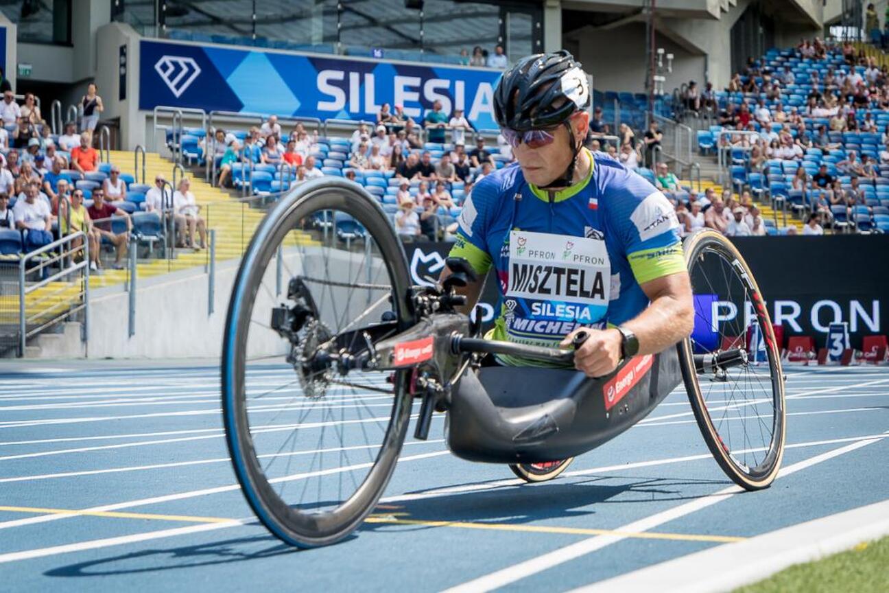 Paralympic athlete in a racing wheelchair competing on a track, Silesia sign visible in the background. (wygenerowano przez AI)