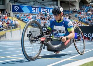 Paralympic athlete in a racing wheelchair competing on a track, Silesia sign visible in the background. (wygenerowano przez AI)