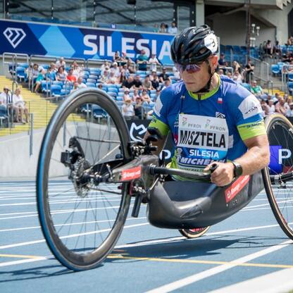 Paralympic athlete in a racing wheelchair competing on a track, Silesia sign visible in the background. (wygenerowano przez AI)