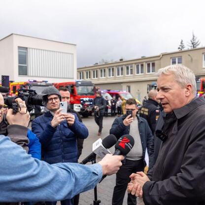 Marszałek Wojciech Saługa wita dziennikarzy podczas ceremonii przekazania nowych wozów strażackich. (wygenerowano przez AI)