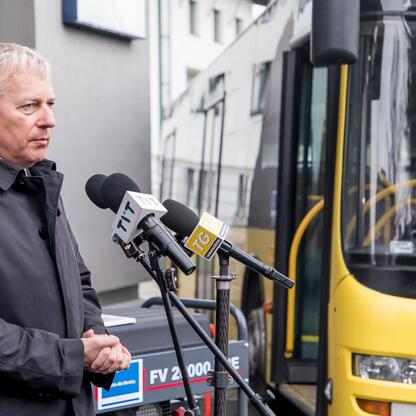 Marszałek Wojciech Saługa przemawia na tle żółtego autobusu, podkreślając znaczenie pomocy dla Ukrainy. (wygenerowano przez AI)