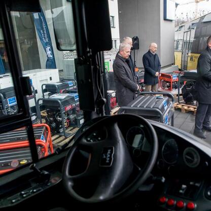 Grupa mężczyzn w strojach formalnych stoi przed autobusem, uczestnicząc w ceremonii przekazania sprzętu do Ukrainy. (wygenerowano przez AI)