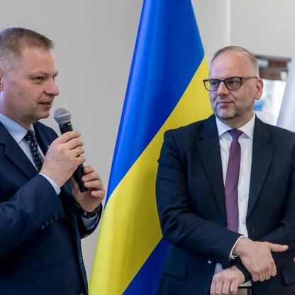 Dwóch mężczyzn w strojach formalnych stoi przed flagami, reprezentującymi Ukrainę i Polskę, podczas dyskusji lub konferencji. (wygenerowano przez AI)