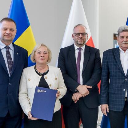 Grupa czterech osób w strojach formalnych stoi przed flagami Ukrainy, Polski i Unii Europejskiej, uczestnicząc w konferencji RLKS. (wygenerowano przez AI)