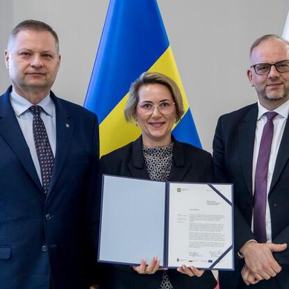 Trzech przedstawicieli z Polski i Ukrainy podpisuje dokument na tle flag, symbolizując współpracę w projekcie RLKS. (wygenerowano przez AI)
