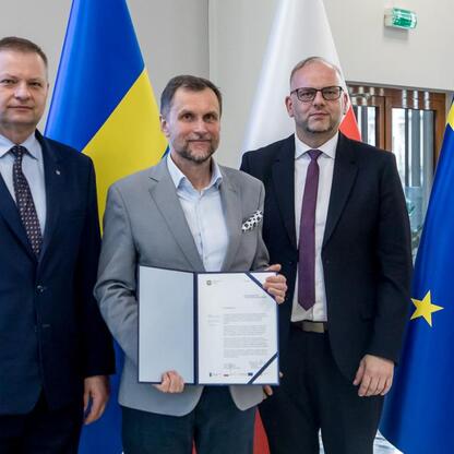 Trzech mężczyzn w strojach formalnych stoi przed flagami ukraińską i europejską, podpisując dokument w ramach inicjatywy RLKS. (wygenerowano przez AI)