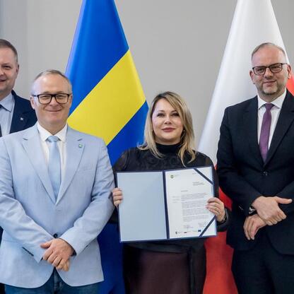 Grupa czterech osób w strojach formalnych, przedstawiających flagi Ukrainy, Polski i Unii Europejskiej, uczestniczących w ceremonii RLKS, wspieranej przez Europejski Fundusz Społeczny Plus. (wygenerowano przez AI)