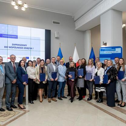 Grupa osób w ścisłym stroju biznesowym z certyfikatami, uczestniczących w uroczystości związanych z projektem Rozwój Lokalny Kierowany przez Społeczność (RLKS) województwa śląskiego. (wygenerowano przez AI)