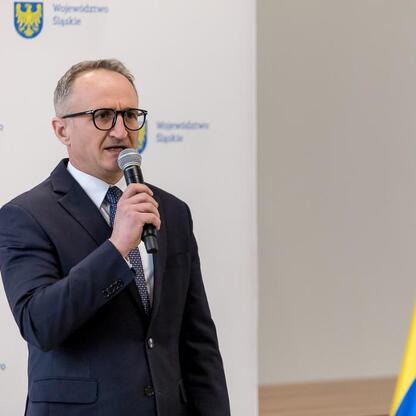 Grzegorz Boski, wicemarszałek Województwa Śląskiego, przemawia na podium podczas uroczystości wsparcia rodzinnych ogrodów działkowych. (wygenerowano przez AI)
