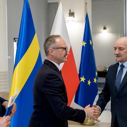 Trzech mężczyzn w strojach formalnych trzyma się za ręce w formalej atmosferze, z flagami Ukrainy, Polski i Unii Europejskiej na tle. (wygenerowano przez AI)