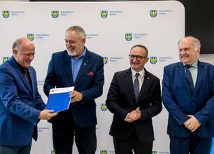 Wicemarszałek Grzegorz Boski przemawia na podium podczas uroczystości finansowej wsparcia dla modernizacji rodzinnych ogrodów działkowych województwa śląskiego. (wygenerowano przez AI)