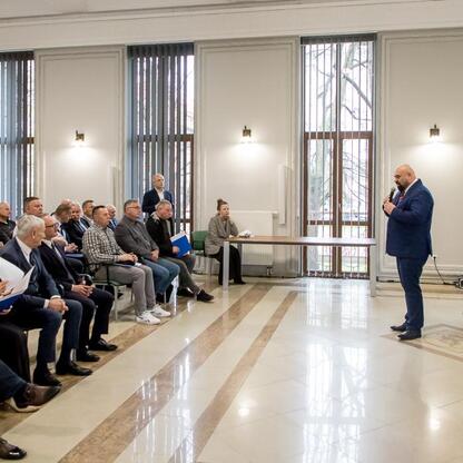 Wicemarszałek Grzegorz Boski przemawia na podium podczas uroczystości finansowej wsparcia dla modernizacji rodzinnych ogrodów działkowych województwa śląskiego. (wygenerowano przez AI)