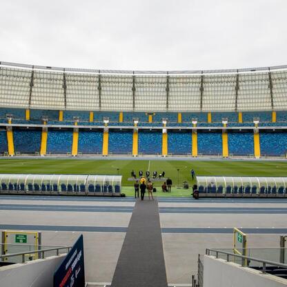 Wnętrze Superauto.pl Stadion Śląskiego, wielofunkcyjnego obiektu w Katowicach, Polska. Puste miejsca, niebieskie i żółte siedzenia, zielona trawa, kilka osób. (wygenerowano przez AI)