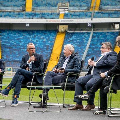 Panel dyskusyjny na Superauto.pl Stadion Śląskim, gdzie Marszałek Województwa Wojciech Saługa i inni dyskutują o potencjalnym organizacji Mistrzostw Europy w Lekkoatletyce w 2028 roku. (wygenerowano przez AI)