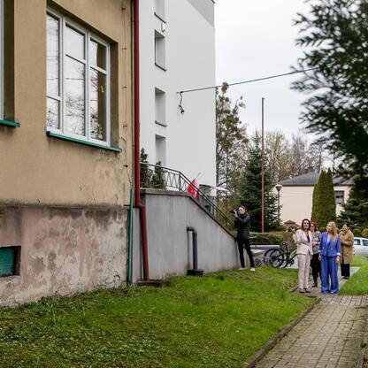 Zebrała się grupa ludzi przed budynkiem szkolnym w Bażanowicach, aby podpisać umowę na budowę nowej sali gimnastycznej. (wygenerowano przez AI)