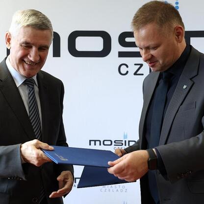 Rafał Adamczyk, Członek Zarządu Województwa Śląskiego, prezentuje dokument na tle MOSiR Czeladz, symbolizując transfer informacji o modernizacji hali sportowej. (wygenerowano przez AI)