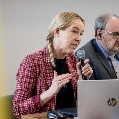 Kobieta prowadzi dyskusję na konferencji, gestykuluje, siedząc obok mężczyzny z mikrofonami i laptopem. (wygenerowano przez AI)