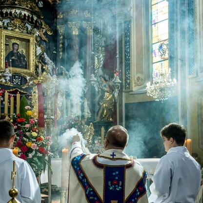 W czasie tradycyjnej inauguracji sezonu pasterskiego w Rychwałdzie na Żywiecczyźnie, w świątyni pełni się ceremonia religijna, podczas której ksiądz i dwa altarzyści w białych szatach wykonują rytuały (wygenerowano przez AI)