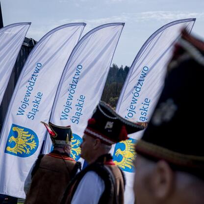 Zapoczątkowano sezon pasterski w Rychwałdzie, Żywiecckie, Śląskie. Grupa w tradycyjnych strojach przemarszuje z flagami Śląskiego Voivodztwa. (wygenerowano przez AI)