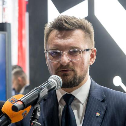 Dwóch uczestników konferencji oświetlonych mikrofonami przedstawiają projekt 