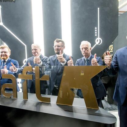 Grupa mężczyzn w garniturach podaje kciuki w stronę oświetlonego logo 