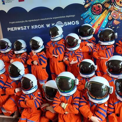 Dzieci w kostiumach astronautów przed kolorowym tłem z napisem 