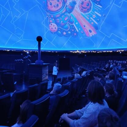 Wnętrze planetarium, dzieci i dorosli uczestniczą w edukacyjnym projekcie 