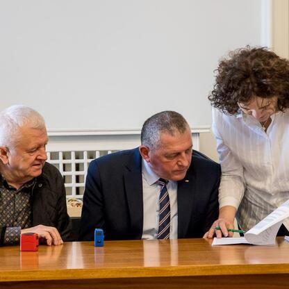 Grupa ludzi w strojach formalnych zgromadzona w pomieszczeniu, omawiając dokumenty, związany z pszczelarstwem i promocją miodu w Śląsku. (wygenerowano przez AI)