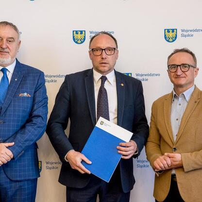 Wicemarszałek Grzegorz Boski prezentuje dokument na tle emblematu Województwa Śląskiego, podczas uroczystości związanych z pszczelarstwem. (wygenerowano przez AI)